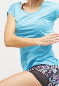 Světle modré sportovní tričko Nike s krátkými rukávy, doplněné vzorovanými černými a barevnými šortkami s vlnitým designem.