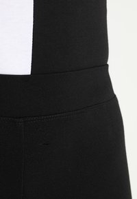 Leggings de sport noirs avec une texture lisse et extensible et une large ceinture. Présente une bande d'accent blanche sur le côté.
