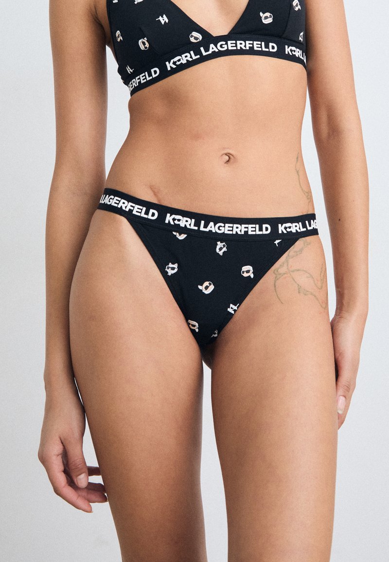 Juodas bikinio komplektas, pasižymintis trikampiu liemenėlės modeliu ir atitinkančiu thong tipo apatiniais. Audinys turi lygų tekstūrą su baltais logotipų raštais.