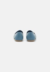 Niebieskie skórzane buty o niskim profilu, zaokrąglonym tylnym pasku i gładkim wykończeniu. Posiadają jasnobrązową podeszwę z minimalnym akcentem designu.