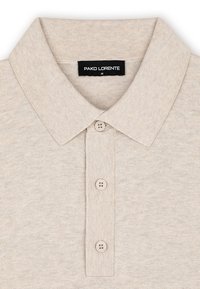 Beżowa koszulka polo wykonana z dzianiny, z zagiętym kołnierzykiem i trzema guzikami. Metka na odzieży wskazuje "PAKO LORENTE," rozmiar M.
