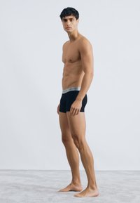 Bóxers negros con una cinturilla gris, diseño ajustado y textura suave, mostrados en una figura masculina sobre un fondo neutro.