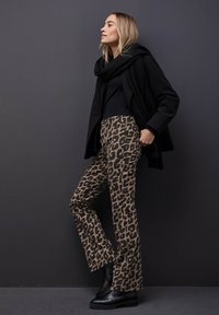 Mustikka huivi, musta toppi, tiukat ruskeat housut mustalla leopardikuviolla ja massiiviset mustat saappaat. Minimalistinen muotoilu tummalla taustalla.