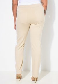 Beige tepláky s bílou krajkovou páskou po stranách, elastickým páskem, dvěma zadními kapsami a zúženými nohavicemi.