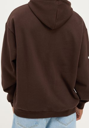 Sudadera marrón con capucha y tela suave y texturizada. Cuenta con un ajuste amplio y una cinturilla elástica. Vista trasera que muestra detalles mínimos en el diseño.