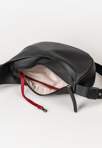Borsa in pelle nera da vita con cerniera aperta che rivela un interno beige decorato e una tracolla rossa con clip metallica.
