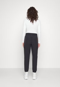 Pantalones cargo negros con cintura elástica, que cuentan con bolsillos laterales y puños ajustados, combinados con una parte superior blanca de manga larga y zapatillas blancas.