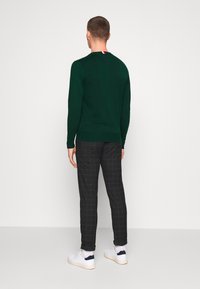 Vihreä neule pitkällisillä hihoilla ja erottuvalla kauluksen nauhalla. Yhdistetty mustiin ruudullisiin housuihin ja valkoisiin tennareihin.