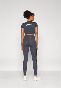 Sivi crop top s "NEBBIA" logom na leđima, u kombinaciji s tajicama visokog struka koje imaju mrežaste bočne panele i glatku teksturu.
