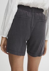 Black elastic-waist shorts with side pockets, textured fabric, and hemmed cuffs. Back view shows two rear pockets and relaxed fit.
