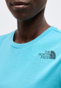 Κοντινή λήψη ενός ατόμου που φοράει ανοιχτό μπλε μπλουζάκι με στρογγυλή λαιμόκοψη και το λογότυπο της The North Face στο στήθος.