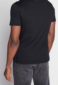Camiseta negra de manga corta, con cuello redondo, ajuste slim, hecha de algodón suave. Combinada con unos vaqueros grises con bolsillos de parche y una textura desgastada.