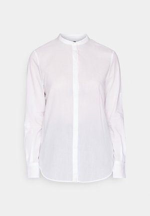 Hvit skjorte med lange ermer og Mandarin krage, frontlukking med knapper og en lett buet kant. Laget av lett, strukturert stoff.