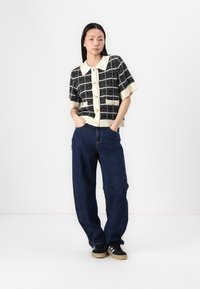 Black and white short-sleeve cardigan with grid pattern, buttons down front, cream collar, paired with loose blue jeans and black sneakers.