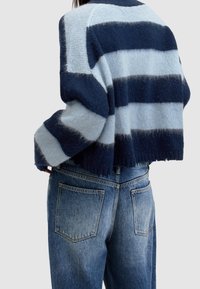 Krótki sweter w granatowo-niebieskie paski, wykonany z miękkiego, teksturowanego materiału. W połączeniu z wysokim stanem, lekko postrzępionymi niebieskimi dżinsami.