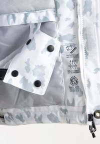 Hvid jakke indvendig med lys grå camouflage mønster, sorte trykknapper, vandtæt og åndbar etiketter, og genanvendt materiale mærke.