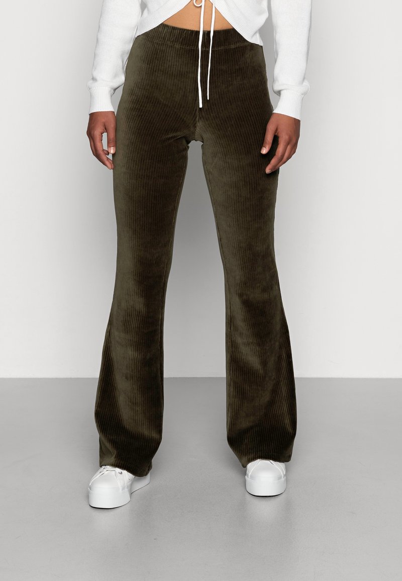 Personne portant un pantalon évasé côtelé vert olive, des baskets blanches à plateforme et un pull court blanc avec des cordons.