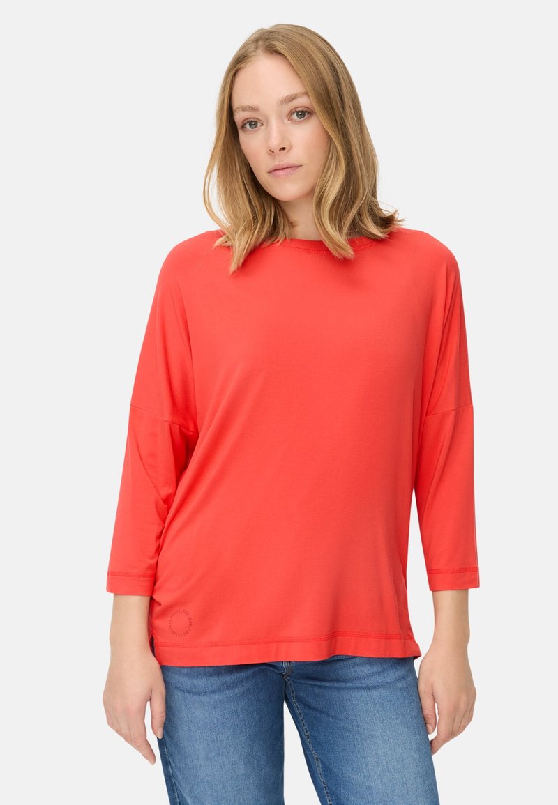 Rød, letvægts, langærmet top med rundt halsudskæring, løs pasform og sidelæg, parret med blå jeans.
