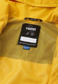 Intérieur d'une veste jaune avec une étiquette noire affichant "reima", des symboles d'entretien et "Conception durable venant de Finlande." Un tissu en maille est visible.