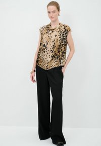 Top de seda con estampado de leopardo y escote drapeado, combinado con pantalones negros de talle alto. Textura suave, ajuste relajado y dobladillo asimétrico.