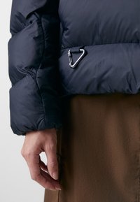 Navy puffer jacket with a quilted texture, featuring a silver metal carabiner accent attached to the waist and a fitted wrist cuff.