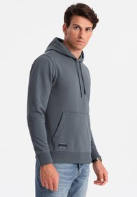 Grijze katoenen hoodie met een vozak pocket, trekkoordcapuchon en geribbelde manchetten. Bevat een klein merklabel aan de zoom. Casual pasvorm.