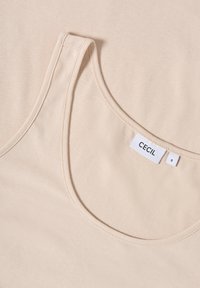 Canotta beige con scollatura rotonda, realizzata in tessuto morbido. Presenta un'etichetta con la scritta "CECIL" e la taglia "S". Texture liscia, design minimale.