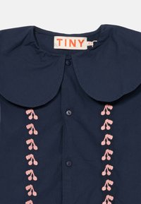 Camicia per bambino di colore blu navy con ampio colletto arrotondato, motivi floreali ricamati in rosa e bottoni blu navy davanti, taglia 4 anni.