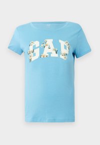 Heleda sinine puuvillane T-särk, millel on valge "GAP" logo lillemotiividega. Lühikesed varrukad ja ümar kaelus. Sile tekstuur.
