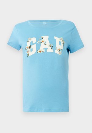 Lyseblå bomull T-skjorte med en hvit "GAP" logo med blomstrete detaljer. Korte ermer og rund hals. Glatt tekstur.