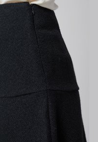 Jupe noire texturée avec taille haute, coutures discrètes et fermeture à glissière sur le côté pour un enfilage facile.