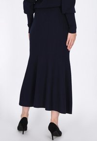 Marineblauwe gebreide rok met een uitlopende zoom, aansluitende taille en textielstof, gecombineerd met zwarte hoge hakken. Achteraanzicht.