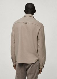 Giacca camicia in misto lana beige con polsino abbottonato e orlo arrotondato, caratterizzata da un colletto semplice e una finitura leggermente textured.