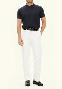 Navy short-sleeve t-shirt, white trousers, black belt, and black loafers. Smooth texture, fitted design, and classic color contrast.