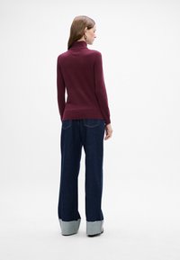 Burgunderfarbener Rollkragenpullover mit langen Ärmeln, kombiniert mit weiten Jeans in Denim mit einem hellblauen Saum und leichter Ausfransung am Ende.