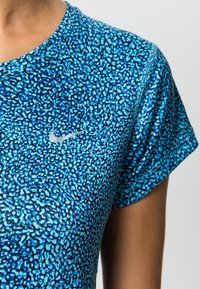 Blå atletisk t-shirt med ett prickigt mönster, korta ärmar, rundad hals och en liten vit Nike-logga framtill. Mjuk, lättviktig tyg.