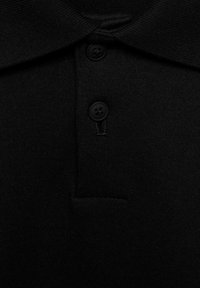 Camisa polo de algodón negra con un cuello estructurado, dos botones negros y un pequeño bolsillo frontal, con una textura suave y uniforme.