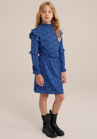 Blåmönstrad klänning med rynkade detaljer och hög krage. Matchas med svarta ankelstövlar. Slät textur med midjeanpassad design.