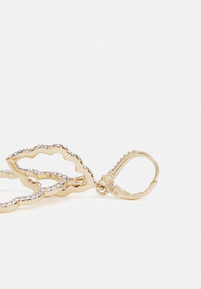 Zlaté kovové náušnice na drátě se vlnitým designem, zdobené malými průhlednými kamínky podél okrajů, obsahující uzávěr.