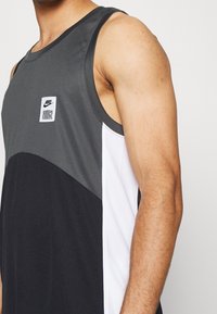 Débardeur de sport gris et noir avec un accent blanc, présentant un tissu texturé et un patch logo Nike sur la poitrine.