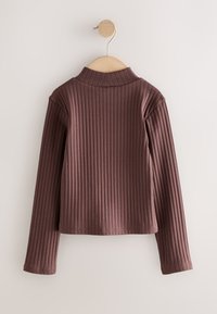 Top marrón oscuro de manga larga con ribetes y cuello alto, de diseño ajustado y dobladillo recto, colgado en una percha de madera.