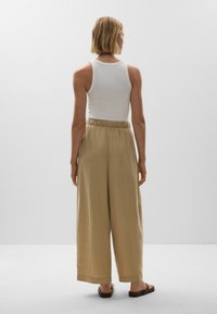 White ribbed tank top paired with loose, tan linen trousers featuring an elastic waistband and wide legs, worn with brown flat sandals.