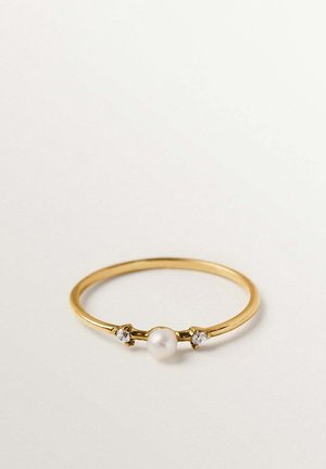 Anillo delgado de oro con una perla blanca central flanqueada por dos pequeñas piedras preciosas claras sobre un fondo blanco liso.