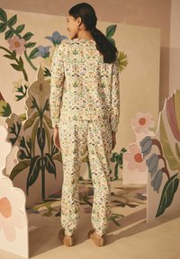 Set di abbigliamento da lounge con motivo floreale in tessuto morbido, caratterizzato da una palette di colori pastello e una vestibilità rilassata. La modella indossa calzature morbide e texturizzate.
