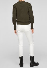 Oliwkowy sweatshirt z bufkami, ściągaczem u dołu i dopasowanymi mankietami, w połączeniu z białymi slim fit jeansami i czarnymi botkami za kostkę.