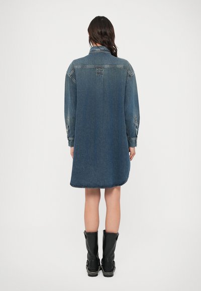 Φόρεμα από τζιν σε σκούρο μπλε με μακριά μανίκια, μανσέτες με κουμπιά και ελαφρώς κυρτή τελική ραφή. Διαθέτει κλασικό γιακά και λεπτομέρεια πίσω στην περιοχή του ώμου.