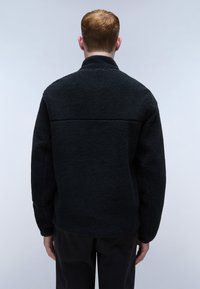 Black fleece jacket with a high collar, textured surface, and long sleeves. Back view shows a seam across the upper shoulder area.