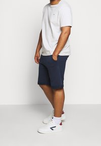 Vit bomullströja, korta ärmar, marinblå shorts, medlängd till låren, med sidofickor, kombinerat med vita sneakers och ankelsockor.