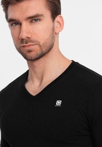 Svart v-ringad t-shirt i mjukt tyg, med en liten vit "ombre" logotyp på vänster bröstområde.