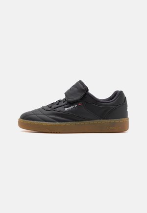 Baskets Reebok en cuir noir avec semelle en gomme marron, devant à lacets, col rembourré et une bande Velcro sur les lacets.